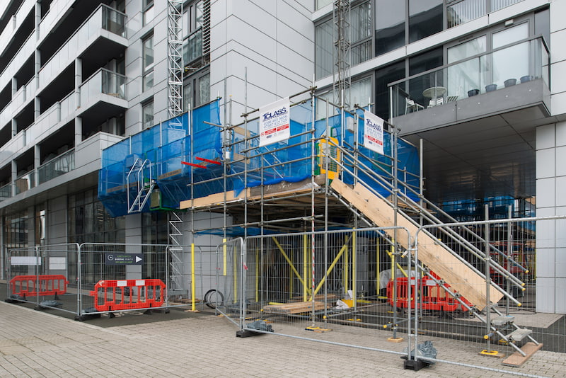 a mast climber alongside scaffolding at the base of a high rise building
